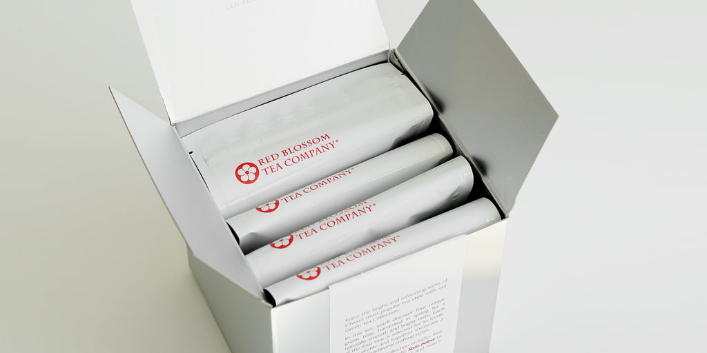 A silver box with 4 white bags of tea showing the Red Blossom Tea Company logo inside.
