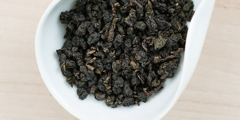 A white dish containing dry Formosa oolong tea leaves.
