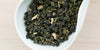A white dish containing dry Formosa oolong tea leaves and pieces of ginseng.