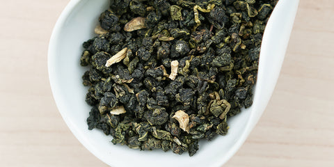 A white dish containing dry Formosa oolong tea leaves and pieces of ginseng.