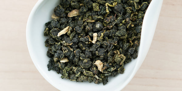 A white dish containing dry Formosa oolong tea leaves and pieces of ginseng.