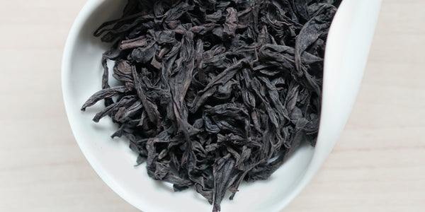 A white dish containing dry Wuyi oolong tea leaves.