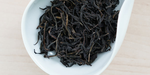 A white dish containing dry Phoenix oolong tea leaves.