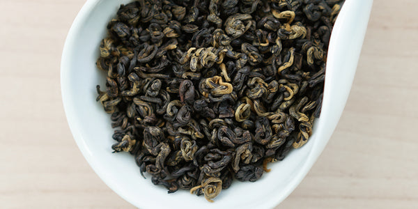 A white dish containing dry black tea leaves.